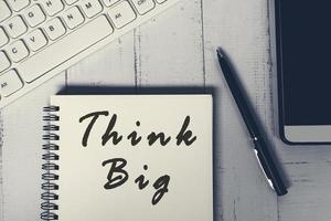Think big word on a notebook with white keyboard, pen, notepad and smartphone. photo