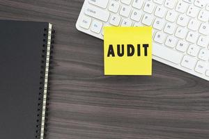 Audit word on adhesive note on top of white keyboard on wooden table. photo