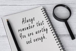 Motivational quote on note book with magnifying glass on white wooden desk. photo