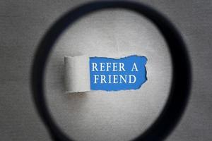 Refer A Friend text on torn paper with magnifying glass. Network concept. photo