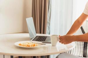 hombre tomando una taza de café con frutas frescas mientras trabaja en una computadora portátil. foto