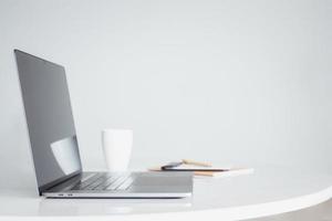 Open laptop computer with coffee and notebook on white table. photo