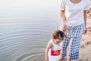 A young mother plays with her 2-5 year old daughter on the beach in summer. Outdoor resort on the lake Have a good rest on weekends, family days. photo