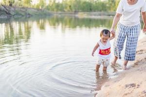 una joven madre juega con su hija de 2 a 5 años en la playa en verano. resort al aire libre en el lago para descansar bien los fines de semana, días familiares. foto