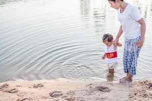 A young mother plays with her 2-5 year old daughter on the beach in summer. Outdoor resort on the lake Have a good rest on weekends, family days. photo