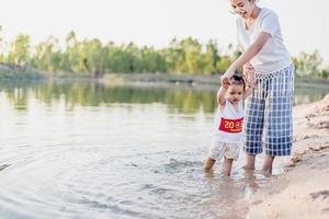 una joven madre juega con su hija de 2 a 5 años en la playa en verano. resort al aire libre en el lago para descansar bien los fines de semana, días familiares. foto