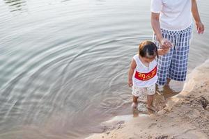 una joven madre juega con su hija de 2 a 5 años en la playa en verano. resort al aire libre en el lago para descansar bien los fines de semana, días familiares. foto