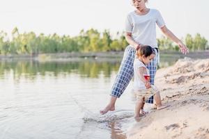 A young mother plays with her 2-5 year old daughter on the beach in summer. Outdoor resort on the lake Have a good rest on weekends, family days. photo