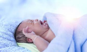 bebé recién nacido llorando recién nacido cansado y hambriento en la cama bajo una manta de punto azul. bebé llorando ropa de cama de bebé, bebé gritando. foto