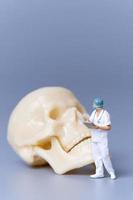 Miniature people Doctor with a giant human skull on a grey background photo