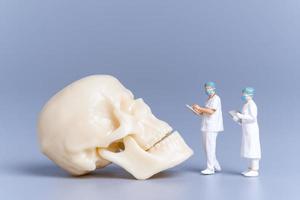 Miniature people Doctor with a giant human skull on a grey background photo