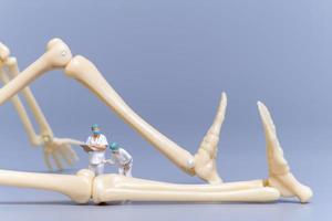 Miniature people Doctor with a giant human bone on a grey background photo