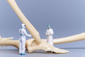 Miniature people Doctor with a giant human bone on a grey background photo