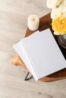 White book blank cover mockup on stylish wooden coffee table with roses bouquet, high angle view photo