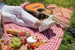 unrecognizable young woman in white pants outside having picnic, eating and playing guitar photo