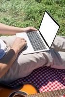 unrecognizable man in white pants outside having picnic and using laptop, working outdoors photo