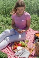 woman in white pants outside having picnic and using smartphone taking photo