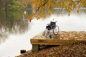 una silla de ruedas vacía en un puente de madera cerca del río en el parque de otoño. el concepto de accesibilidad de las personas con discapacidad. foto