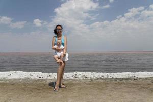 A beautiful woman and her little son are hugging tightly against a blue sky with clouds and a pink sea. Traveling with children. photo