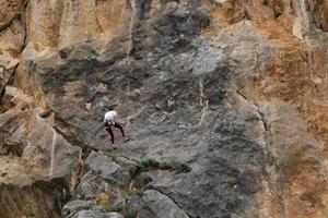 A young girl, an athlete, a rock climber on a sheer red rock. The concept of active, extreme recreation and hobbies. View from the back. photo