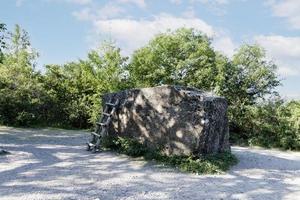 A large, huge stone megalith with a staircase against the background of green trees and a blue sky, used as an observation deck. photo