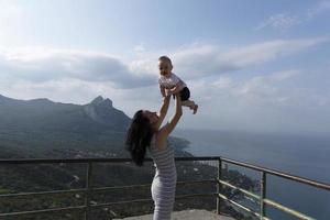A beautiful woman and her little son rise in their arms against the backdrop of rocky mountains, sea and sky with clouds. Traveling with children. photo