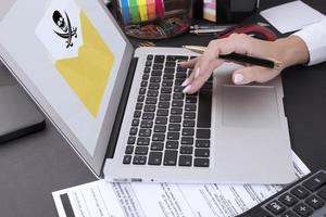 Female hands with a manicure on a laptop keyboard and a warning on a computer screen, an envelope with a skull and crossbones. the system is hacked. photo