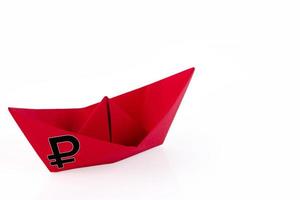 Red paper boat with the symbol of the Russian ruble on a white background. The concept of a Russian warship is going to the bottom. photo