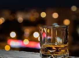 whisky de malta en un vaso de whisky en una noche de verano con el bokeh de la ciudad en el fondo