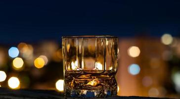 Single malt whiskey in a whiskey glass on a summer night with the city bokeh in the background photo