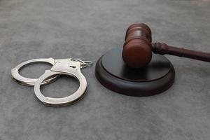 Law theme. Court of law trial in session. Judge gavel handcuffs on grey table in lawyer office or court session. Mallet of judge on concrete stone grey background. Justice human rights concept. photo