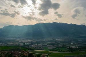 Mountain landscape, cloudy open sky, vineyards in the distance and rays of sunshine in the clouds photo