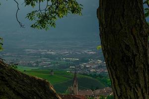 Rural village with church framed between trees, mountain environment with sunset's light filtered by plants photo