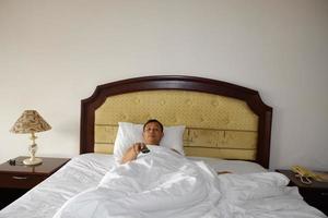 Man watching TV in his bed hand holding a remote control. photo