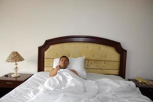 Man watching TV in his bed hand holding a remote control. photo