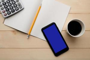 Top view with copy space of wooden working table with calculator, paper cup of hot coffee, yellow pencil, notebook, smartphone. photo