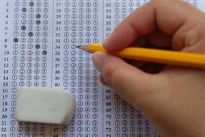 Close up and top view of Answers sheet with blue sharp pencil in hand and rubber isolated on white background. Top view of them. Take the exam timely concept. Selective focus photo