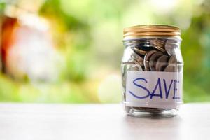 Coins and text SAVE in a glass jar placed on a wooden table. Concept of saving money for investment and emergency situations Close up, Blurred background photo