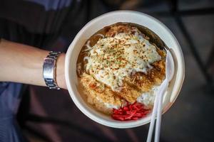 Tonkatsu traditional Japanese food, crispy fried pork with sauces on top and rice under it, in the paper dish. Food street of Bangkok, Thailand. photo