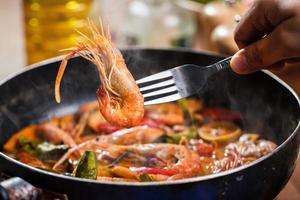 Tom Yum Goong or Tom Yum Kung, Thai hot and sour shrimp soup in pan. Thai food in Thai cuisine restaurant. Use a fork to lift the shrimp out of the pan. Shrimp and Spices in coconut milk. Closeup photo