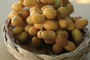 los dátiles amarillos maduros se cultivan orgánicamente, son dulces, deliciosos y frescos en una cesta tejida sobre un fondo azul y blanco con las manos de un hombre sosteniéndolos. foto