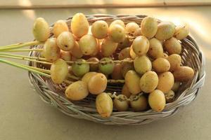 ripe yellow dates are organically grown, sweet and delicious and fresh in a woven basket on a blue and white background with the hands of a man holding them. photo