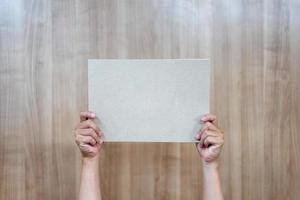 Asian person is holding and raising up the empty a4 paper on the wood background. photo