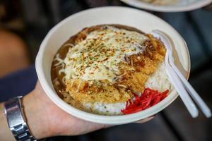 Tonkatsu traditional Japanese food, crispy fried pork with sauces on top and rice under it, in the paper dish. Food street of Bangkok, Thailand. photo