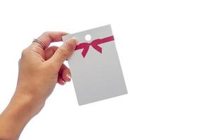 mano de mujer sosteniendo la tarjeta de papel blanco con un lazo rojo. es una imagen aislada en la pantalla blanca. foto