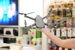 Asian woman hand hold the Gray Drone in blur electronic store. photo