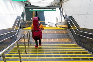 chico japonés bajando las escaleras en la estación de tren con la mochila de guitarra en la espalda. foto