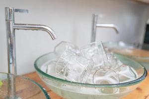 mucho vaso de agua en el fregadero de cristal listo para lavar y limpiar. foto