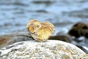 Heart shape stone against background of beach. Summer sunny day. Love, wedding and Valentine day concept. Finding beautiful and interesting stones. Beach vacation. photo