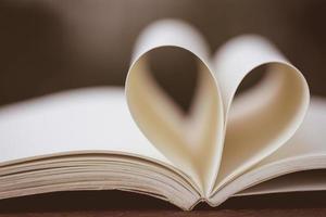 Close up heart shape from paper book on wooden table with vintage blur background photo